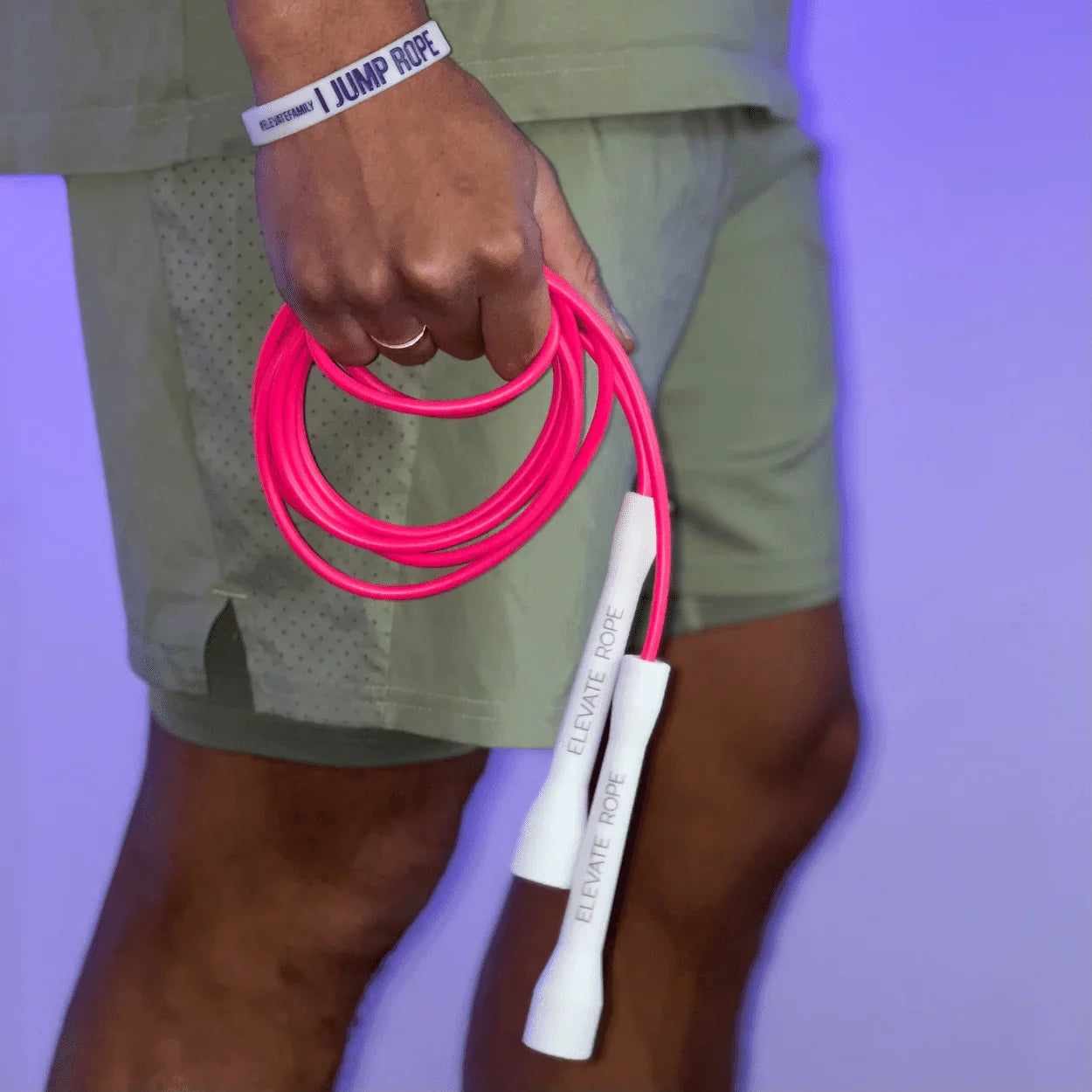 Person holding bright pink jump rope with white handles, wearing 'I JUMP ROPE' wristband for fitness training