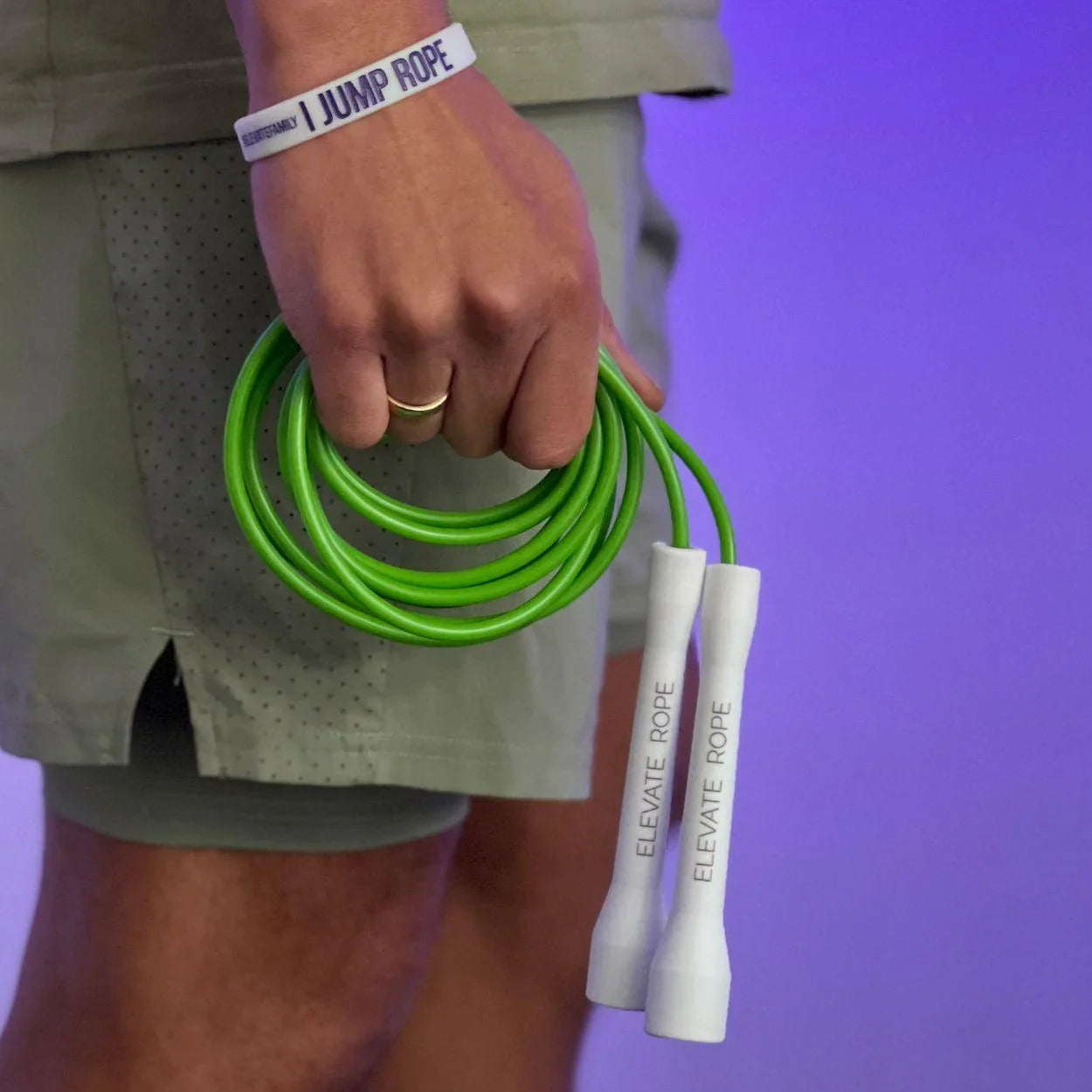 Hand holding bright green jump rope with white handles, wearing 'I JUMP ROPE' wristband for fitness training.